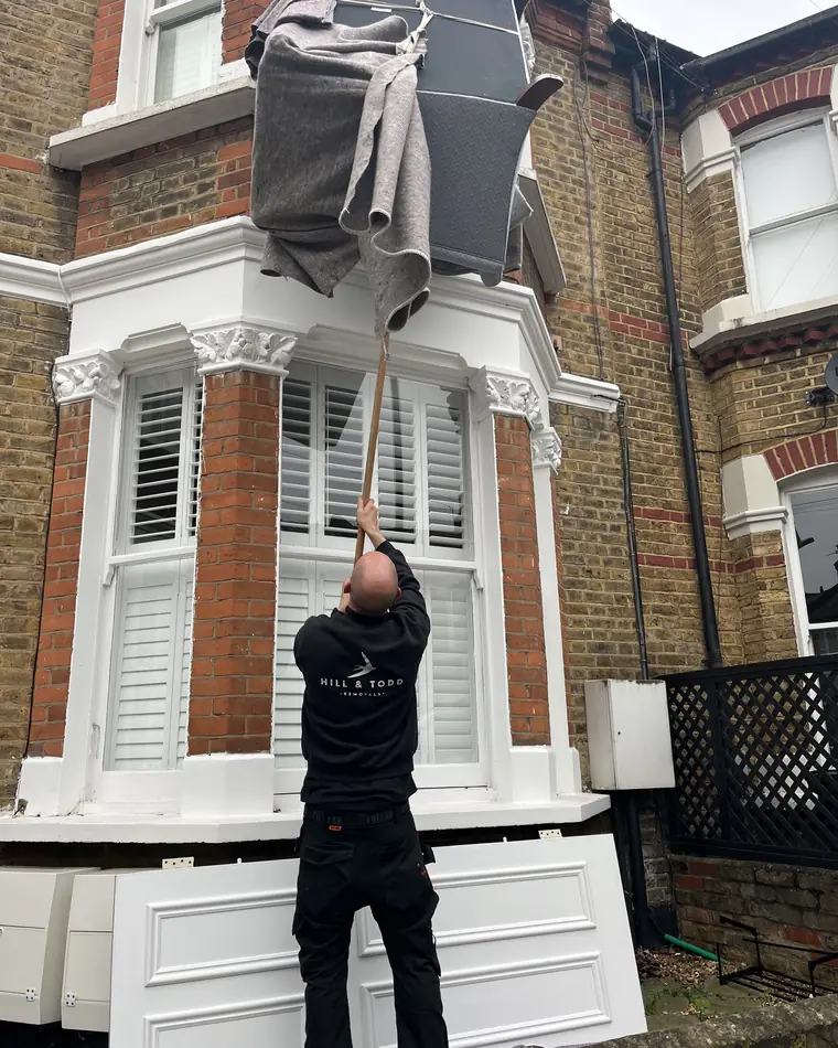 A Hill and Todd mover on the ground guiding a wrapped sofa up the front of a London terrace