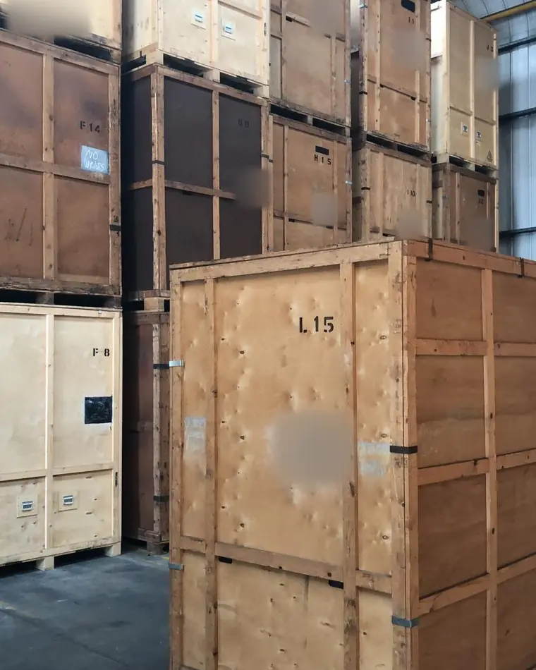 Stacked wooden storage containers in a warehouse, each marked with its container number